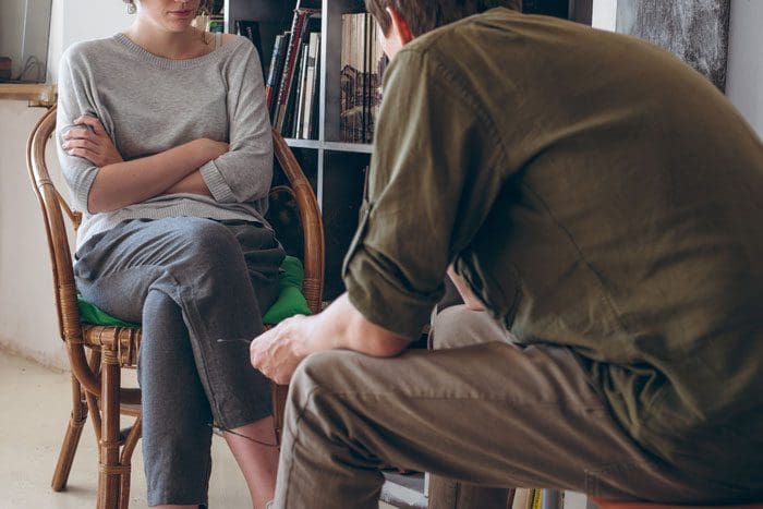 Approaching-Family-Members-with-Love-and-When-to-Contact-an-Interventionist - man talking to woman both sitting in chairs by bookcase