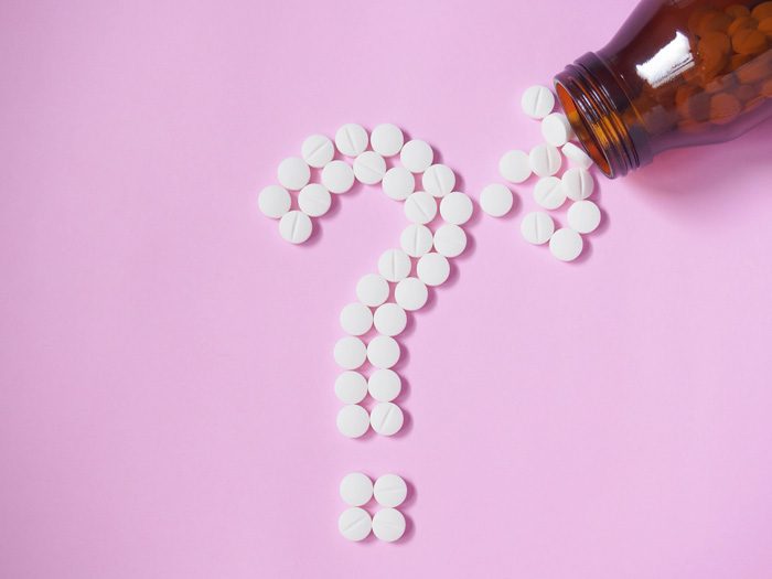 white pills laying in shape of question mark on pink paper