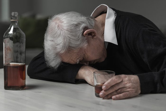 very old man drinking whisky with head down on his arm - older adults