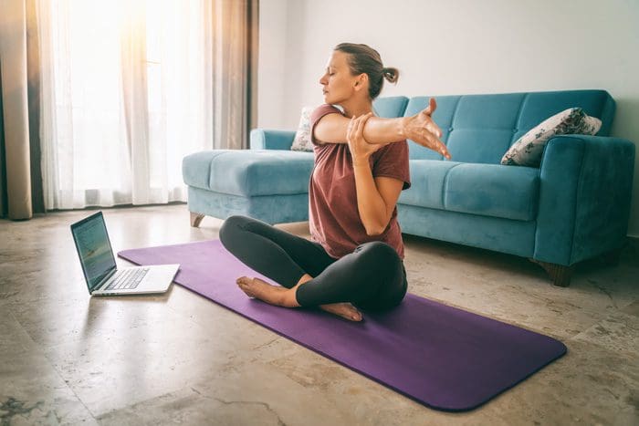 woman stretching on mat at home in front of laptop - quit drinking