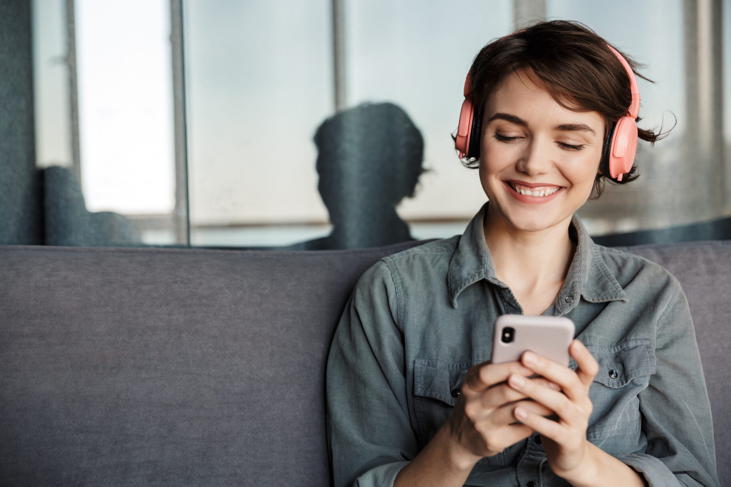 Image of nice young smiling woman using smartphone and headphone, 10 Podcasts That Add to Your Motivation, Motivational podcasts, Image of nice young smiling woman using smartphone and headphone