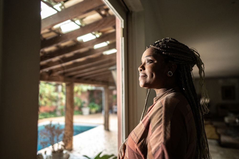 Recovery Expecataions(1000 x 667 px) A woman stands by a window, looking outside with a calm and hopeful expression, symbolizing reflection and progress in recovery.