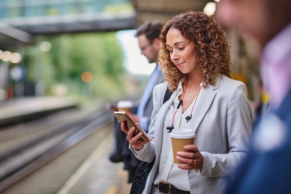 Great Oaks – Why a News Fast Might Help Your Mind and Body – Edited Great Oaks - Why a News Fast Might Help Your Mind and Body - Edited. A woman stands on a train platform reading and smiling at her phone.